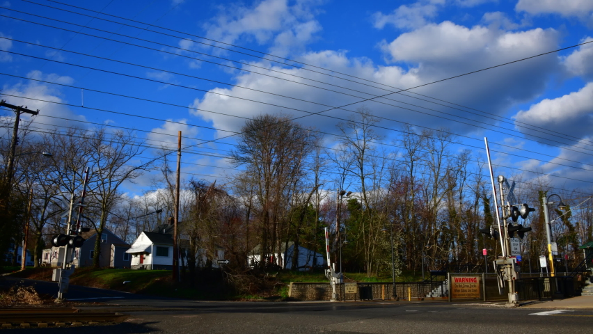 Small town suburban NJ train crossing during rush hour on a beautiful late afternoon at rush hour with blue sky and billowy white clouds and trees.