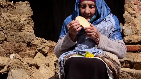 Bread in grandmother's old hands. Grandmother eats bread against the backdrop of slums. Need food. Hunger and poverty. Old grandmother with a piece of bread on the background of ruins