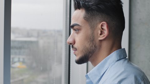 Portrait serious focused arabic guy man Hispanic male student boss businessman leader in shirt stands in office looking out window thinking about problem solution dreaming about future plans planning