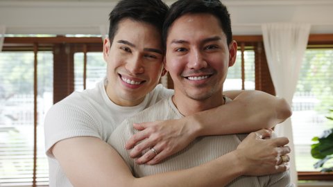 Portrait Young Asia Gay couple feeling happy smiling at home. Asian LGBTQ men relax toothy smile looking to camera while hug in living room at home in the morning concept.