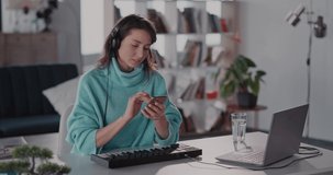 Caucasian young woman in headphones listening music and using smartphone social media typing messages.Communications. Electronic keyboard. Staying home.