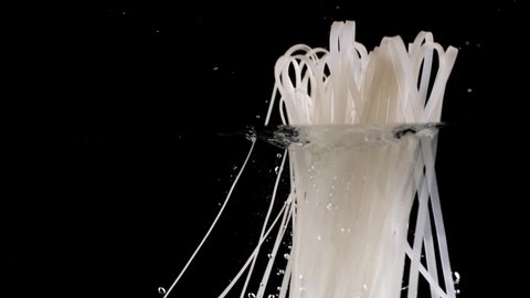 Dropping noodles into a pot of clean boiling water on black background in slow motion.