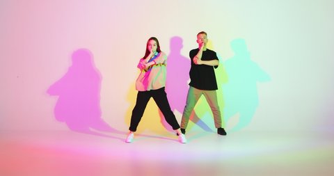Cool dancing young couple synchronously moving in colourful studio light. Contemporary dance, hip hop dancers