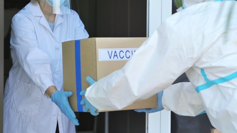 covid-19 coronavirus vaccine delivery,healthcare workers in protective suit and mask unloading medical goods boxes to hospital doorstep