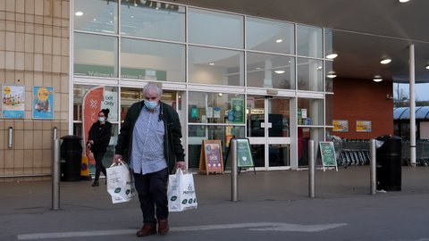 SALFORD, MANCHESTER, UNITED KINGDOM - CIRCA APRIL, 2021: Customers wearing protective face masks entering and exiting Morrisons supermarket. Outdoor scene at entrance door.