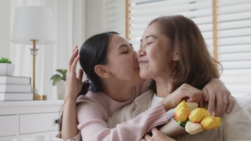 Attractive beautiful asian middle age mum sit with grown up daughter give gift box and flower in family moment celebrate mother day. Overjoy bonding cheerful kid embrace relationship with retired mom. Royalty-Free Stock Footage #1071686476