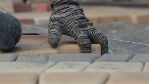4K Details with hands of a mason working with cobblestone . Construction worker laying paving slabs on the street. Engineer on protective gloves makes the sidewalk , hitting stone with hammer 
