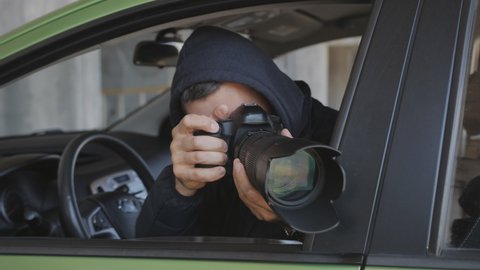 A private detective or photojournalist secretly takes photos from a car window with a long-focus lens.