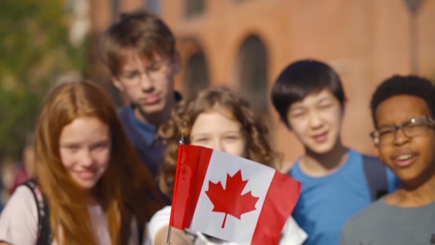 Group of adorable mixed race schoolkids with Canadian flag outside school building. Portrait of multiethnic classmates from school in canada posing outdoors