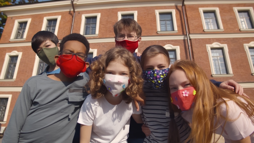 Low angle view of diverse school students wearing colorful protective mask looking at camera. Portrait of multiethnic preteen students in safety mask posing at camera outside school building Royalty-Free Stock Footage #1071691810