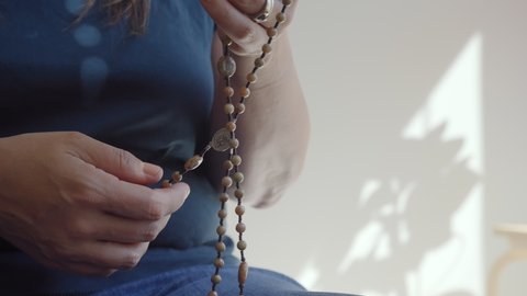 Detail of woman's hand counting through stone Rosary beads next to a window, 4K UHD
