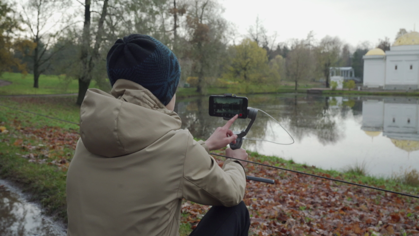 Vlogger boy with mobile phone camera stabilizer recording outdoor video blog in autumn park. Teenager shooting video for travel vlogging. Catherine Park, Tsarskoye Selo, Saint Petersburg, Russia.