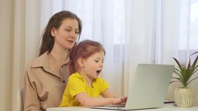 A woman works from home with her child. Family look at the screen of the tablet and the TV together. Caucasian mother working from home, having a work video call, daughter playing nearby.