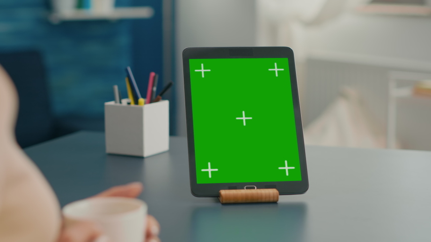 Close up of tablet computer with mock up green screen chroma key display it is used for office work. Freelancer woman working on communication project using isolayed gadget sitting on desk