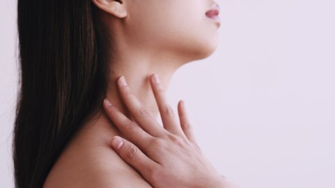 Beauty care. Skin treatment. Wellness rejuvenation. Profile portrait of brunette Asian woman touching smooth soft neck bare shoulders applying lotion with fingers isolated on light background.
