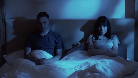 Couple problem. Night conflict. Relationship issue. Disappointed mad wife upset husband siting in bad ignoring each other late in bed in dark home bedroom with blue moonlight.