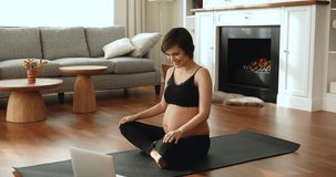 Young pregnant woman wear activewear sit on mat in modern living room in front of laptop watch online training class repeat exercises, prepare body for childbirth feels healthy, pregnancy yoga concept