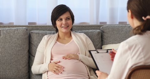Pregnant woman having obstetrician midwife doctor appointment, young female patient sit on sofa at clinic office answers gynecologist question. Prenatal care check-up, keep unborn baby healthy concept