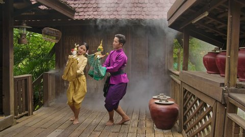 Slow motion beautiful asian male and female traditional colorful dress on Ayutthaya Bangkok cultural fashion clothes holding handicraft toy doll puppet dancing on the old wooden house floor 