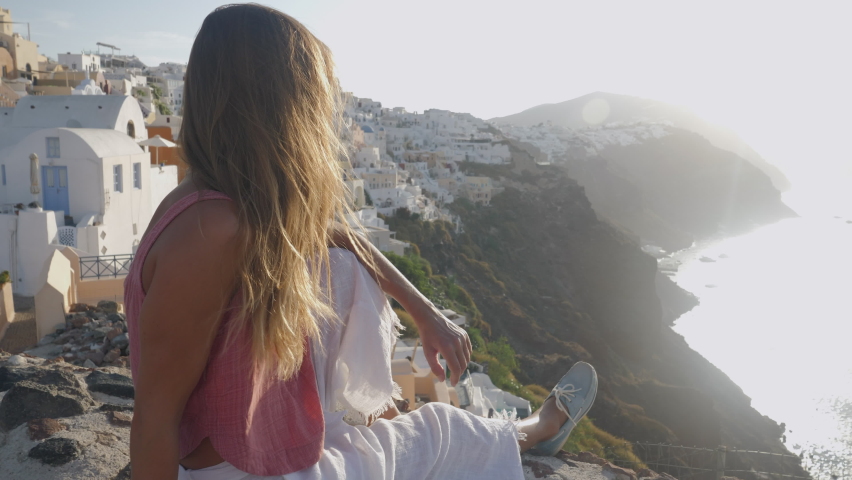 Slow motion: Young woman traveller in Santorini, Greece takes a moment to enjoy sunset and stunning Greek island view  | Shutterstock HD Video #1071719422