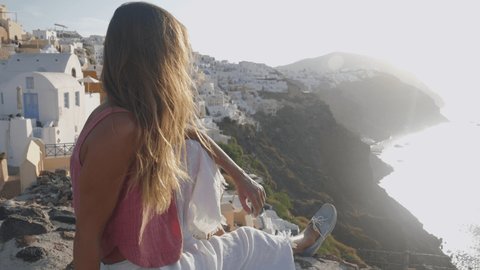 Slow motion: Young woman traveller in Santorini, Greece takes a moment to enjoy sunset and stunning Greek island view 