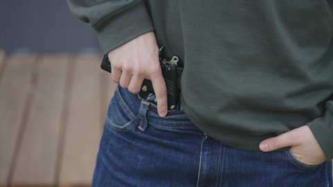 The man is hiding the gun in his pants. Illegal carrying of firearms