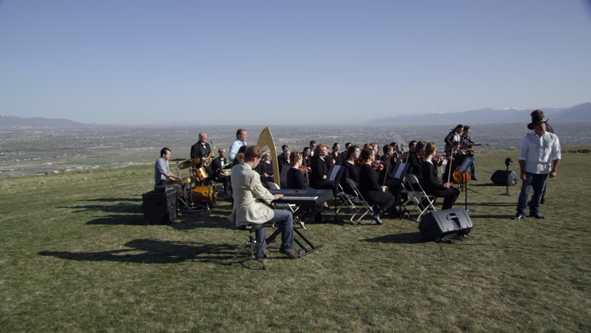 Orchestra performing outdoors on a hill overlooking a valley.