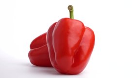 Video of two red bell peppers slowly turned on a white background.