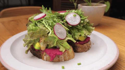 Close up of plant based sandwich with beetroot spread topped with loads of green leaves and radish