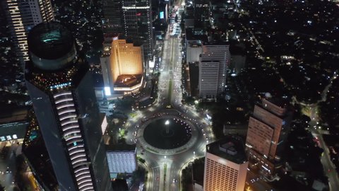 Aerial night drone view closing in on Selamat Datang Monument roundabout with fast car traffic in Jakarta, Indonesia
