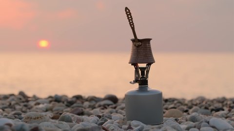 Cooking turkish coffee in cezve on the portable gas camping stove on empty beach at sunrise in Turkey. 