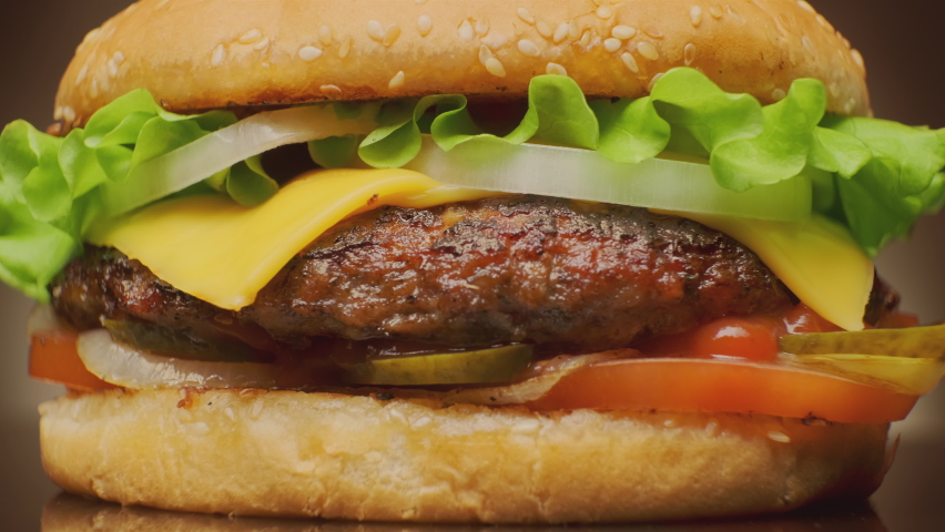 Juicy beef burger with cheese and fresh vegetables rotating on table close up, fast food.
