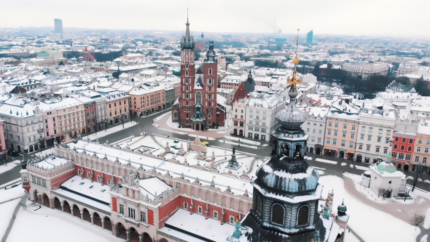 Slow motion footage of Basilica of Saint Mary and Medieval Main market square, Cloth Hall and Town Hall Tower. Winter season in the old town of Kralow, Poland. City skyline. Snow-covered buildings. 