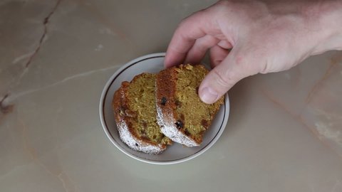 The man takes a piece of homemade muffin and takes a bite of it.Homemade cakes on a saucer.Orange raisin muffin.Breakfast, snack.
