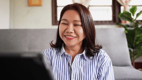slow motion scene of young asian woman sit inside living room and using digital tablet to video call to greeting friends for VOIP network technology life concept