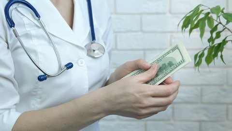 Doctor earn money. A female doctor in medical uniform count money in her hands.