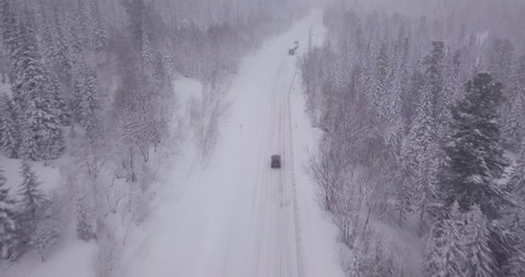 Black car rides on a snowy road in the taiga in the forest in snowfall winter