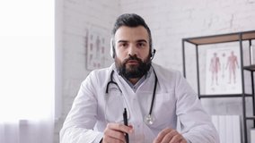 Male doctor wearing white coat consulting patient remote online using headset,diagnosing and giving treatment recommendation. Medical assistant has video call,conference with colleagues.Webcam view
