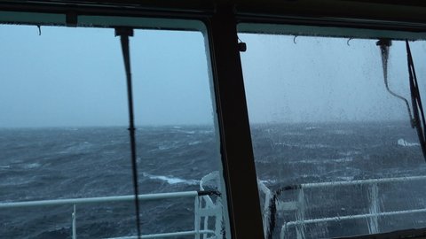 View from ship's bridge. Storm. Ship is rocking. High waves. White foam on the water. Windshield wiper works.