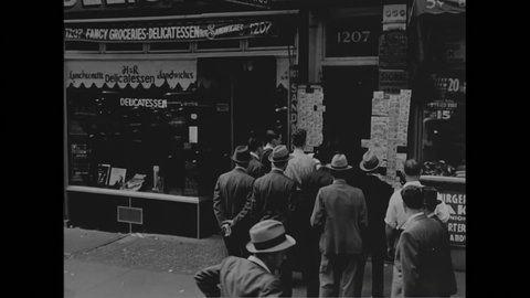1940s: Men sit on city stoop playing cards. Busy city street. Men gathered outside of storefront.
