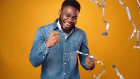 Cheerful young african man jumping and dancing with joy under falling party confetti against yellow background - Powered by Shutterstock - Get 15% off with code: PIKWIZARD15