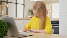 Blonde girl doing homework at home on a laptop. Online learning, distance lesson, education at home, technology for schoolboy, business conference. Children doing homework at home. Back to School.