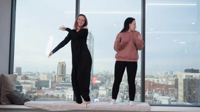 Two girl's girlfriends cheerfully dance standing on the windowsill with panoramic views of the big city. High quality 4k footage