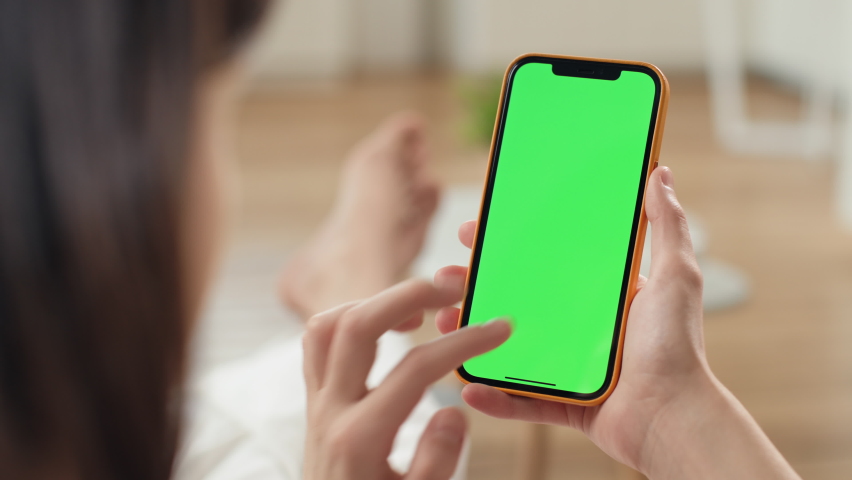 Russia - February 17 2021: Use green screen for copy space closeup. Chroma key mock-up on smartphone in hand. Woman holds mobile phone and taps to click or answer video call indoors of cozy home
