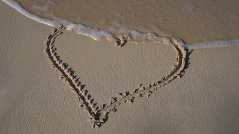 Wave comes and erase drawing of Hart in the sand. Concept of relationship and togetherness