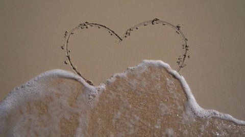 Wave comes and draw the Hart on the sand. Concept of beginning relationship and togetherness