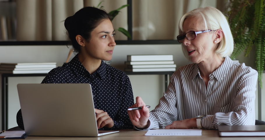 Concentrated older senior hoary businesswoman leader discussing online project on computer with motivated young indian ethnicity colleague, brainstorming ideas or problem solution at office meeting. Royalty-Free Stock Footage #1071788500
