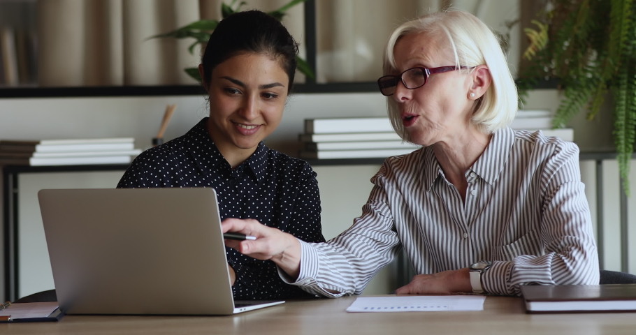 Concentrated older senior hoary businesswoman leader discussing online project on computer with motivated young indian ethnicity colleague, brainstorming ideas or problem solution at office meeting. Royalty-Free Stock Footage #1071788500