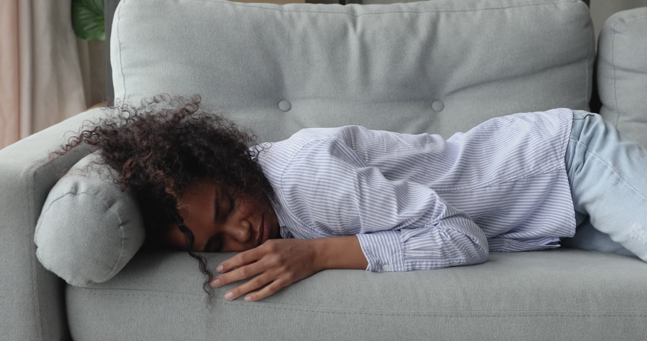 Young African ethnicity woman feels tired like squeezed lemon, without motivation and energy, fall down on sofa in living room at home. Exhausted overworked female, hard working day, breakdown concept | Shutterstock HD Video #1071788635