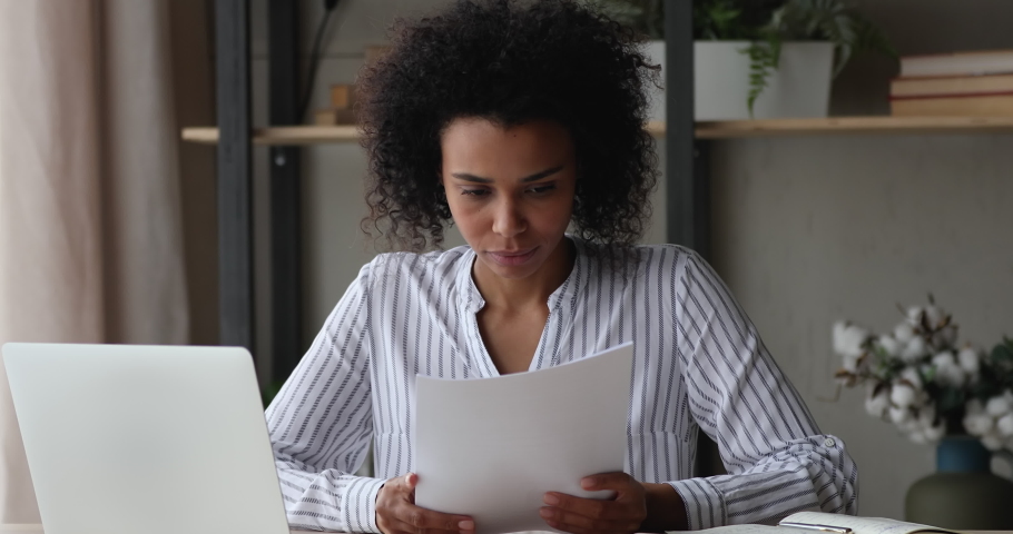 African woman sit at workplace desk holding papers reading bad news in letter feels frustrated concerned due high taxes, loan debt, dismissal, staff cuts notice, debt eviction notification concept Royalty-Free Stock Footage #1071788662